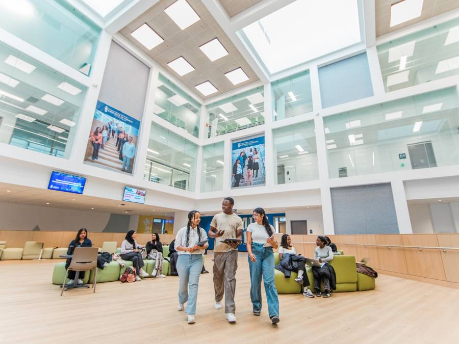 Students walking and sitting in a bright, modern campus building with large windows and high ceilings